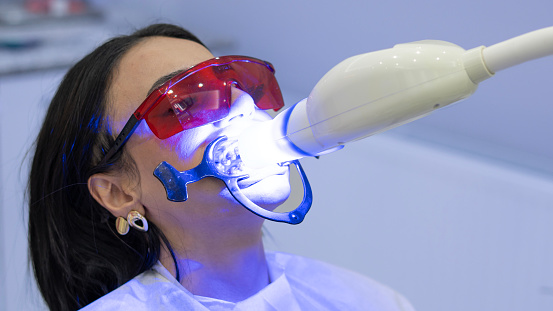 Woman getting dental treatment with UV light in dental clinic