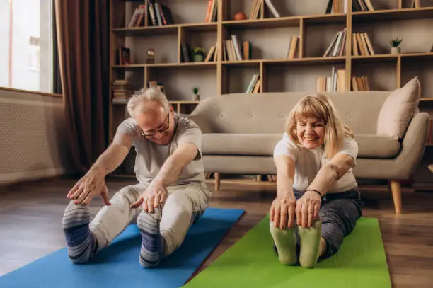 Active and focused senior couple doing the stretching while practicing yoga together in their living room at home