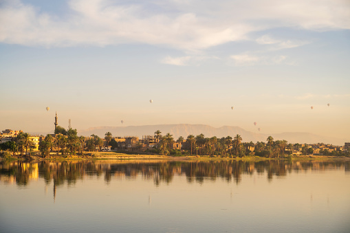 Idyllic scene as the calm waters of the River Nile reflect the buildings on the riverbank in the early morning sunshine. Luxor, Upper Egypt.