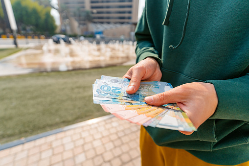 Young man holding Kuwaiti dinar on the street in Kuwait City in Kuwait. Close-up.