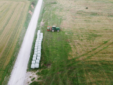 Aerial view of a tractor on a field with bales wrapped in plastic