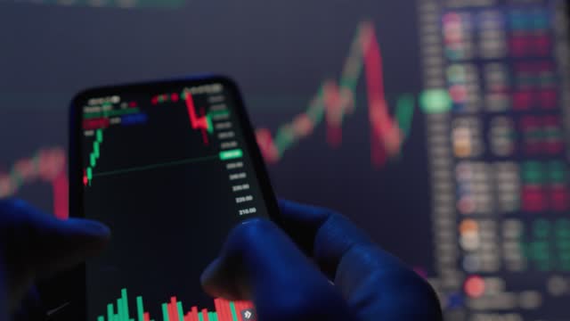 It is easy and convenient to analyze and manage your investments simply using your smartphone. See how hands hold a smartphone and perform trading operations on online charts.