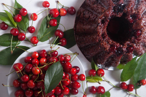Delicious chocolate cake with sweet cherry, white plate with berry of sweet cherry and green leaves of cherry tree on white background.