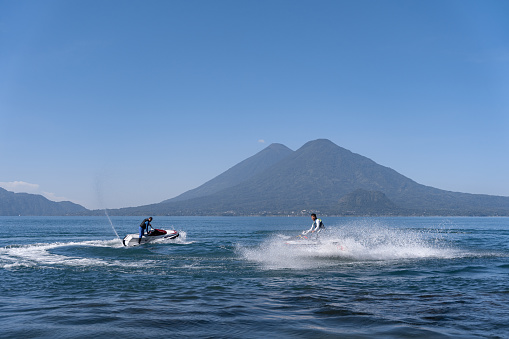 Two young Hispanic men navigate jet-skis on the waters of Atitlan Lake, Guatemala, engaging in recreational water activity against the scenic backdrop of the lake's natural beauty