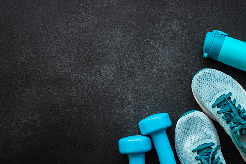 Workout and fitness concept, sport equipment. Sneakers, dumbbels and water bottle at black background. Flat lay with copy space.