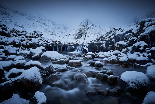 Fairy Pools, Glen Brittle, Isle of Skye during winter. All rocks and the mountains are covered with snow on a grey December day.