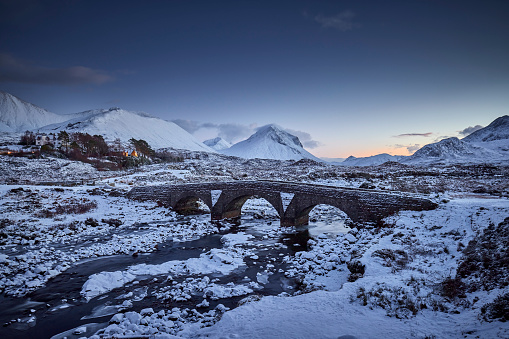 Sligachan old Bridge, Isle Of Skye, Scotland. Sligachan bridge during sunset, the water flows quickly under the bridge. In the background you can see the mountains on Skye that are covered in snow.