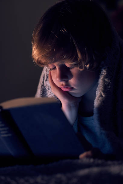 istock Cute boy reading boy in dark room 1989937022