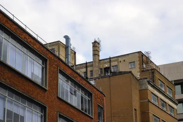 Street-level daytime view of mid-sized brick-built commercial building exteriors in Whitechapel, London. Rooftop details show railings, external ladders, chimneys and air-conditioning vents.