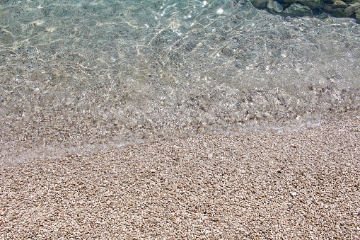 Small Pebbles On The Seashore. Small Pebbles On Beach. Clear Sea Water. Blue Mediterranean Sea.