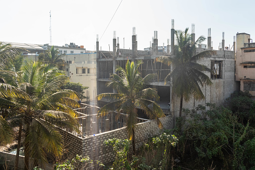 Hassan, Karnataka, India - January 10 2023: Overlooking a construction site surrounded by several residential buildings and green palm trees against a sunny sky