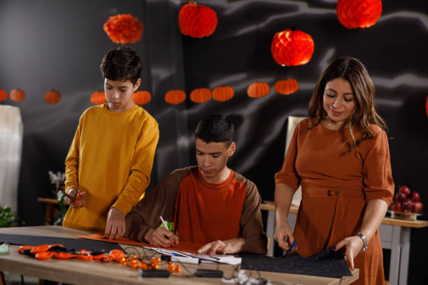 mother and two sons making paper halloween decorations - 12 15 months foto e immagini stock