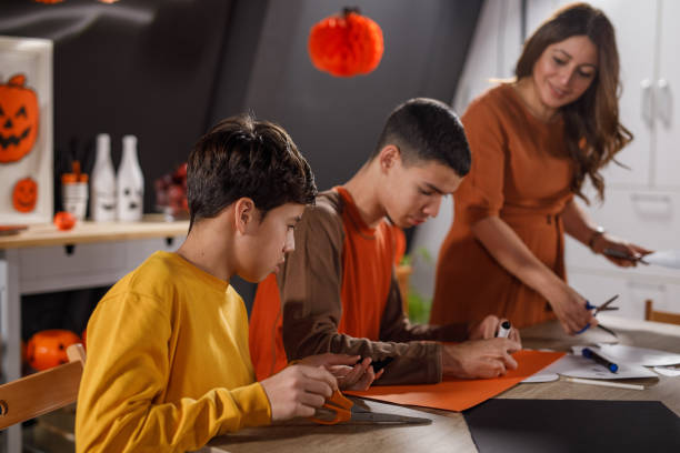 mother and two sons making paper halloween decorations - 12 15 months foto e immagini stock