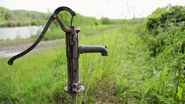 A water pouring out of deep well faucet standing near a lake in grass