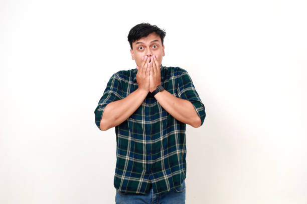 istock Shocked young handsome asian man standing while covering his mouth. Isolated on white 1990005962