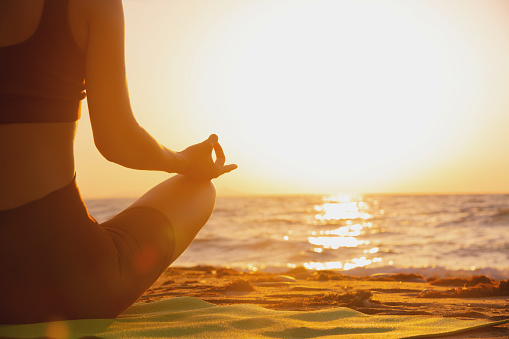 Young woman doing yoga on the beach during a sunset. Silhouette of an unrecognizable female.