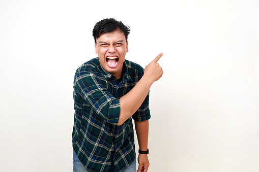 Young asian man laughing while pointing sideways, Isolated on white