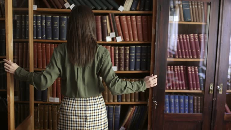 Beautiful young woman opening bookshelf to take a book in library