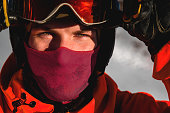 guy in ski goggles adjusts them on his face and wearing a protective helmet, close-up. A male skier has the sun shining on his face and stands against the backdrop of high mountains. Winter sport