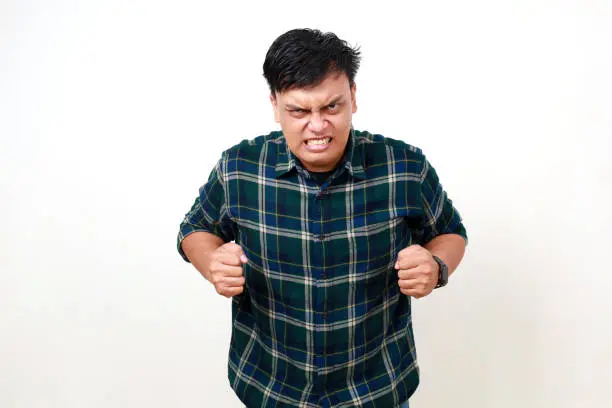 Annoyed and angry asian young man raising hands and clench teeth outraged, stare pissed-off at camera, going to kill someone, standing on white background