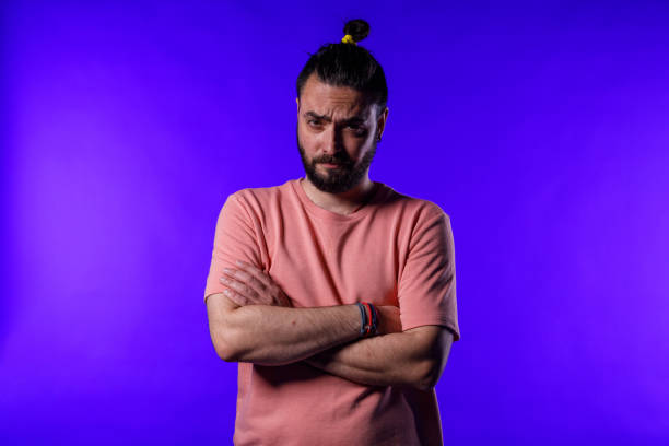 Portrait of serious mid adult hipster standing against bright blue background, arms crossed, frowning while looking at camera.
