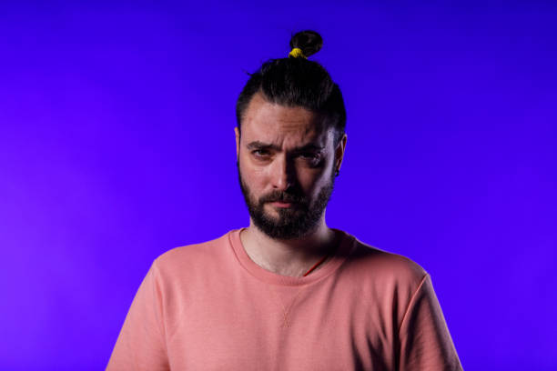 Portrait of serious mid adult hipster standing against bright blue background, frowning while looking at camera.