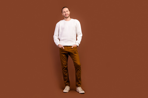 Full length photo of good mood cheerful man wear white sweater smiling empty space isolated brown color background.