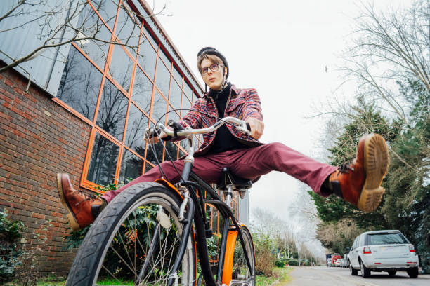 male student in helmet on cruiser bicycle spreading wide legs and screaming when riding bike on urban sidewalk. no traffic jams, eco friendly transportation for carbon footprint. sustainable lifestyle - daily cruiser imagens e fotografias de stock