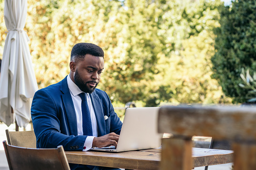 Business black man in suit working with laptop in outdoor cafe