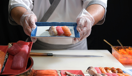 A skilled sushi chef proudly presenting a beautifully arranged plate of delicious sushi, demonstrating the artistry and precision involved in the culinary world.
