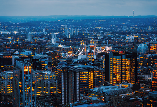 Panoramic aerial night view after sunset to the cityscape of London with Tower Bridge and the illuminated skyscrapers of the city during dusk in the United Kingdom