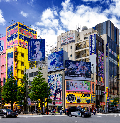 Tokyo, Japan, April 29 2023  - Image of a street crossing in Ahikabara, many comic and Hentai advertising on the colourful buildings visible, taxi and car in the foreground, pedestrians visible on the sidewalk