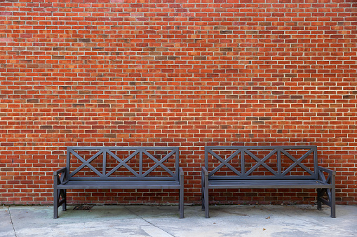 Two iron black benches sit against a brick exterior wall of a building providing copy space and background.