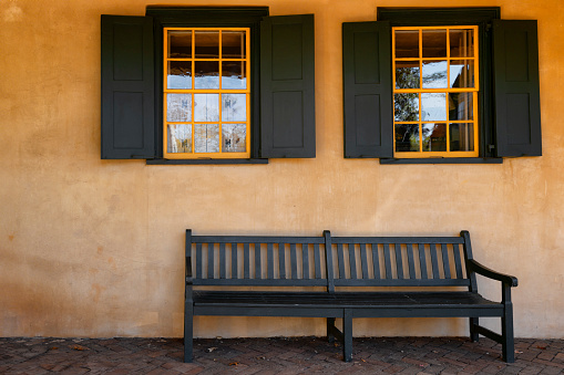 Exterior wall of a building with two windows, shutters matching bench that sits below them.