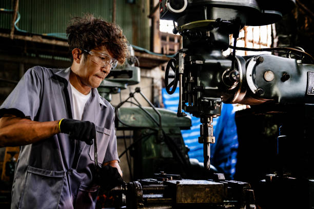istock Engineer worker in production plant drilling at machine. Professional worker near drilling machine on factory. man inspecting and repairing machine for operation in workshop. 1990183053