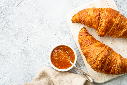 Croissant with jam on cutting board at stone table top view. Traditional snack or breakfast.
