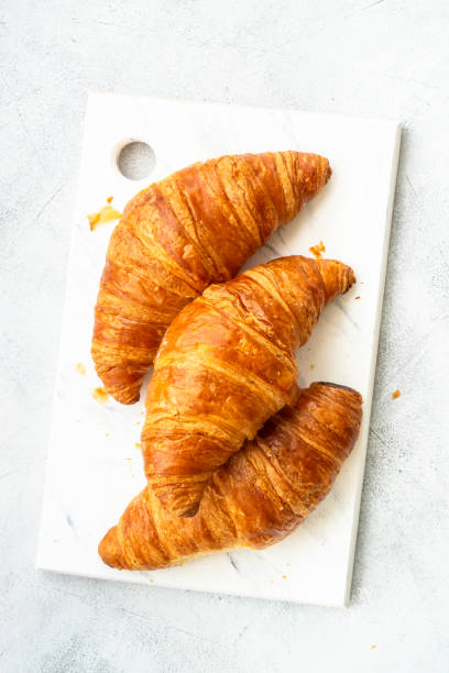 istock Croissant on cutting board at white table top view. 1990225120