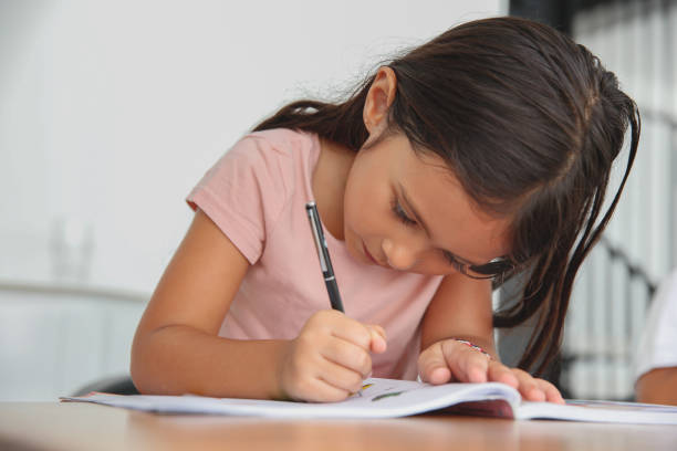 Close-up shot of homeschooling little girl doing homework and study alone. She's writing on her textbook.