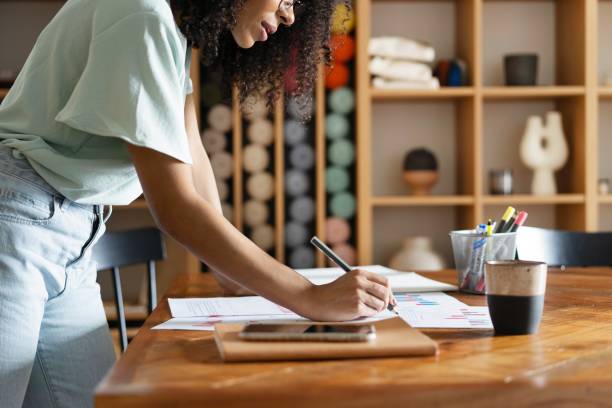 istock Young designer work project. Photo woman working with new startup project in modern loft. Generic design notebook on wood table 1990320454