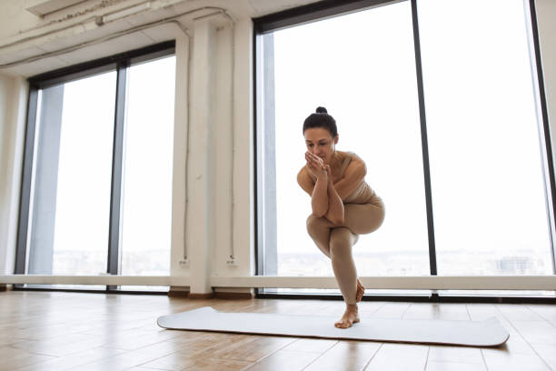 istock Lady balancing on one leg and keeping hands in namaste gesture at training room. 1990328736
