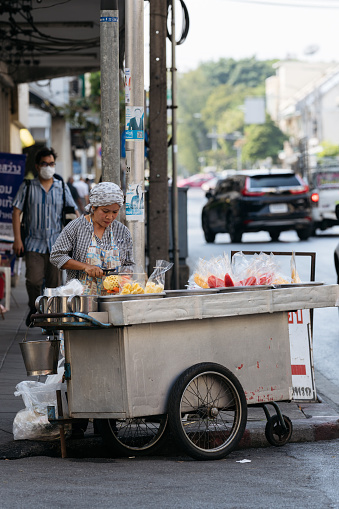 Bangkok, Thailand - 26 January 2024: Woman prepares tropical fruits on a busy street cart