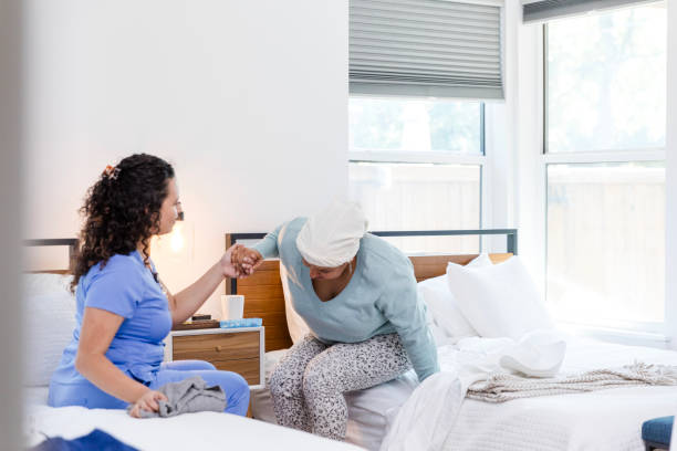 istock Female aide helps weak female patient stand from bed 1990336495