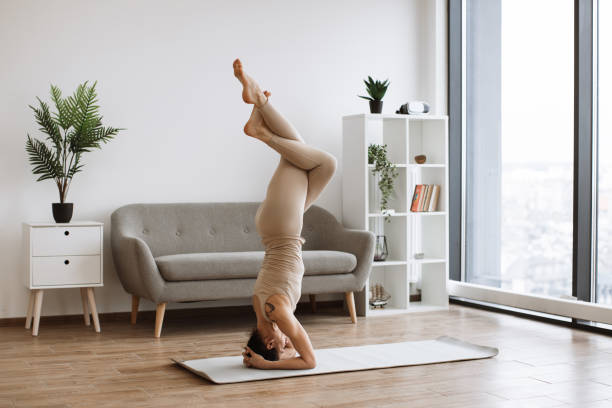 istock Brunette staying in headstand pose at bright commodious living room. 1990342880