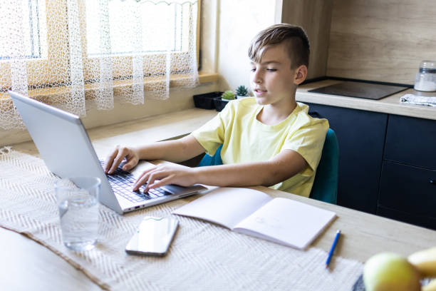 istock Schoolboy is chatting online with his classmates while doing his homework at the kitchen dining table. 1990356220