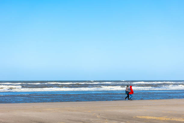 Egmond aan Zee, Netherlands - March 17, 2022: wide sandy beach in the sun with two people along a rough sea