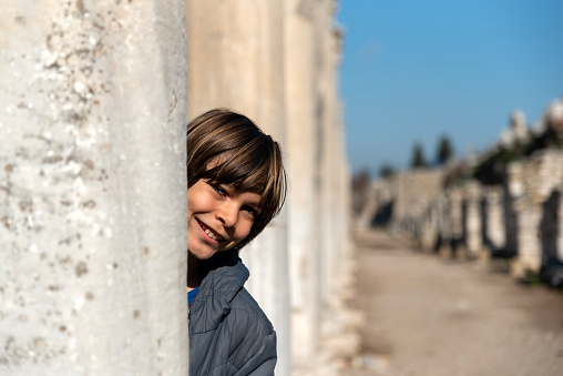 cute little boy hiding behind historical columns and smiling