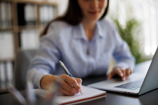 istock Businesswoman taking notes in notebook while working on laptop in the office 1990386439