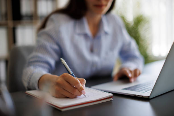 istock Businesswoman taking notes in notebook while working on laptop in the office 1990386440