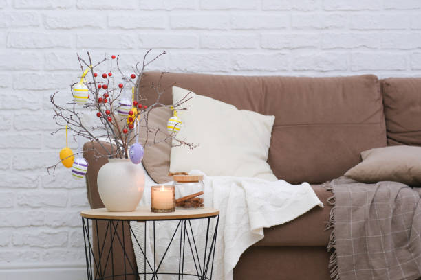 istock Vase with tree branches, Easter eggs and burning candle on table near the sofa in living room 1990402702