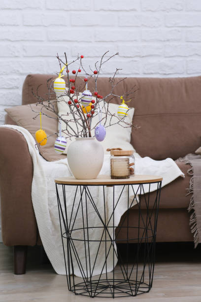 istock Vase with tree branches, Easter eggs and burning candle on table near the sofa in living room 1990412415